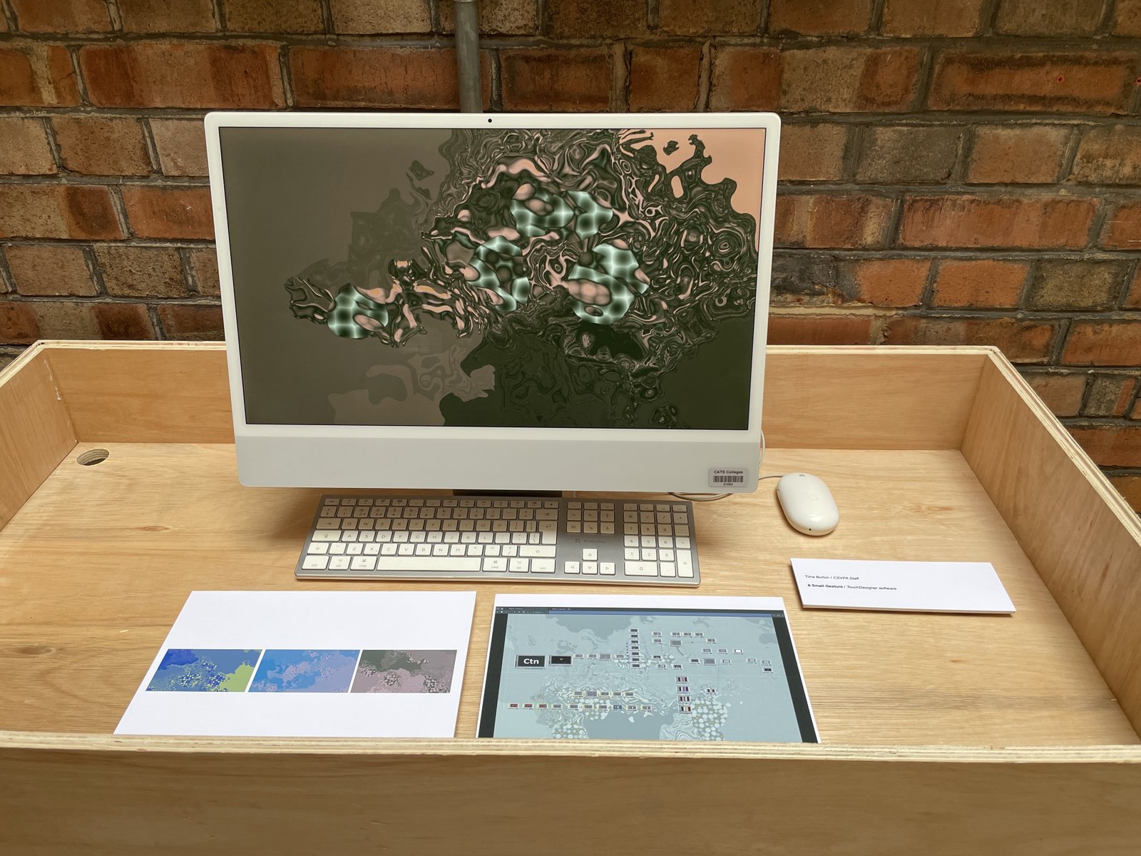 An image of the artwork on a computer, on a desk with artwork caption.